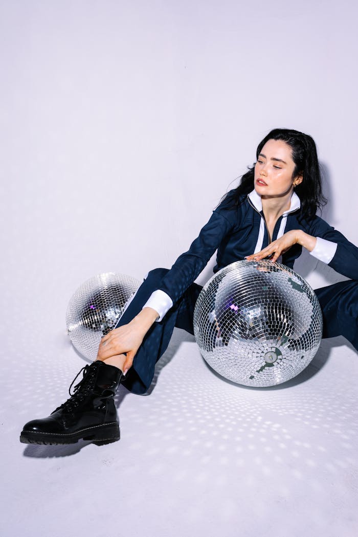 Fashionable woman in a suit posing with disco balls, exuding 80s retro vibe.